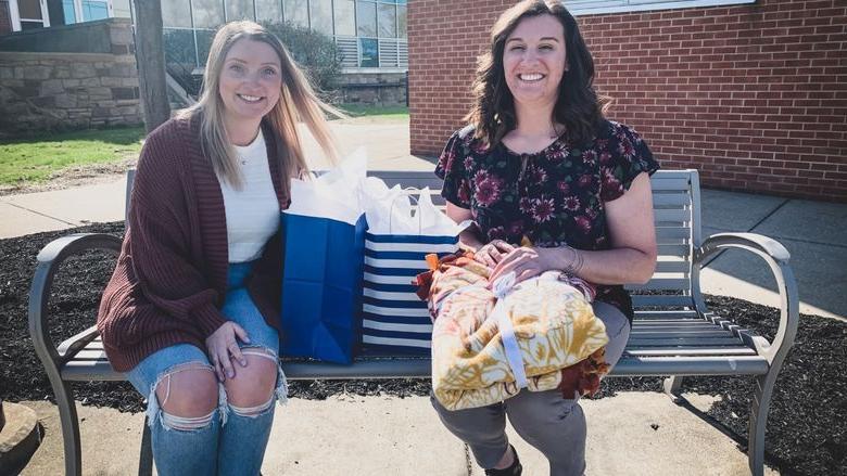 two women sit on a bench exchanging gifts