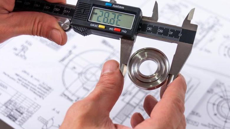 A quality engineer measuring a production part with calipers to ensure its compliance, 在后台有一个参考图.