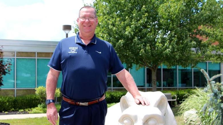 New head golf coach at 365英国上市杜波依斯分校 John Schneider stands with the Lion Shrine on campus.