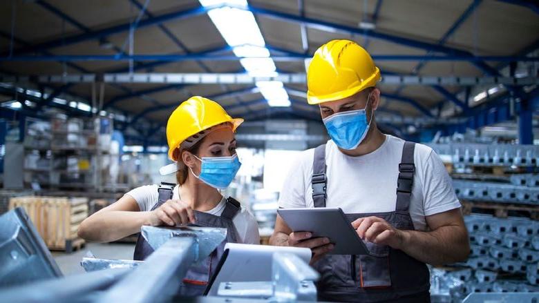 Two masked manufacturing workers in a manufacturing/factory setting