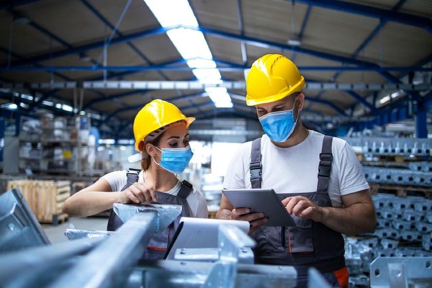 Two masked manufacturing workers in a manufacturing/factory setting